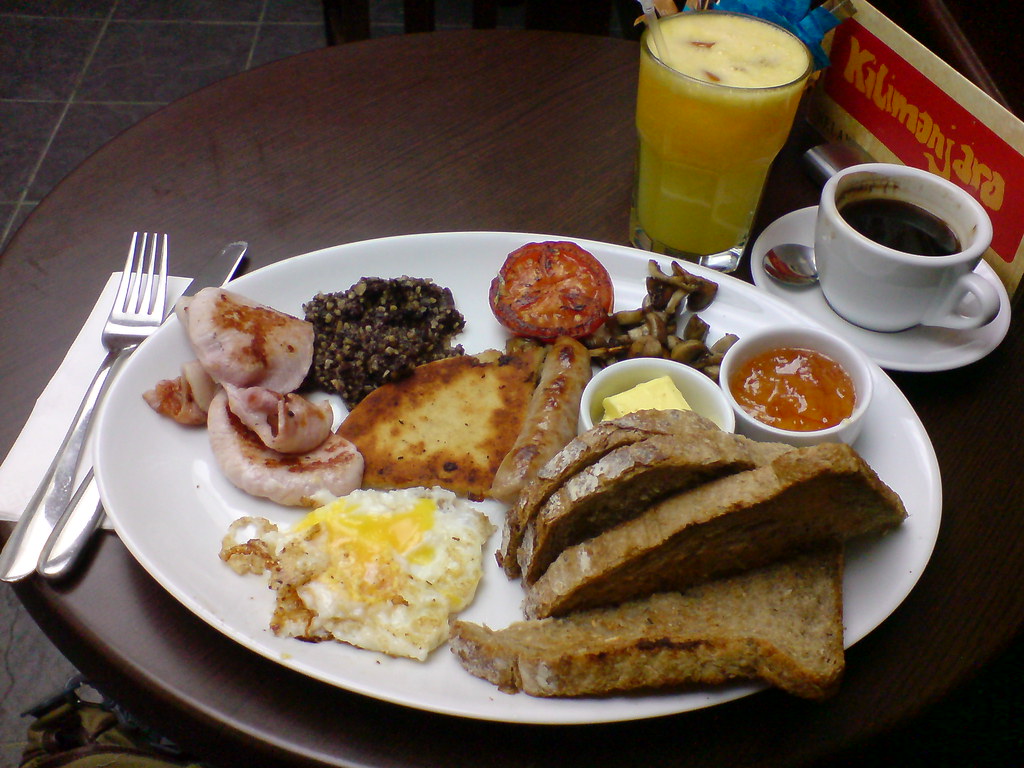 Traditional Breakfast in the UK - roasted tomato, cooked mushrooms, ham, haggis, sausage, fried egg, hash browns, toast, butter, marmalade, espresso, orange juice